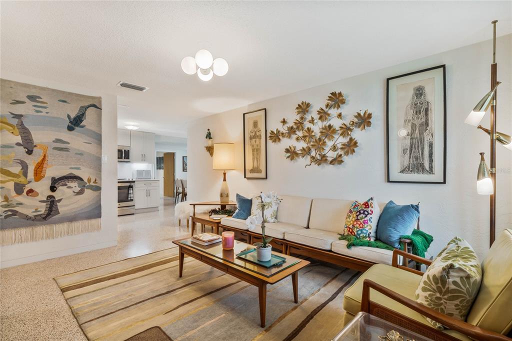 A mid-century modern living room features a wooden sofa, patterned rug, and wall art — 809 E 15TH AVENUE, NEW SMYRNA BEACH, FL