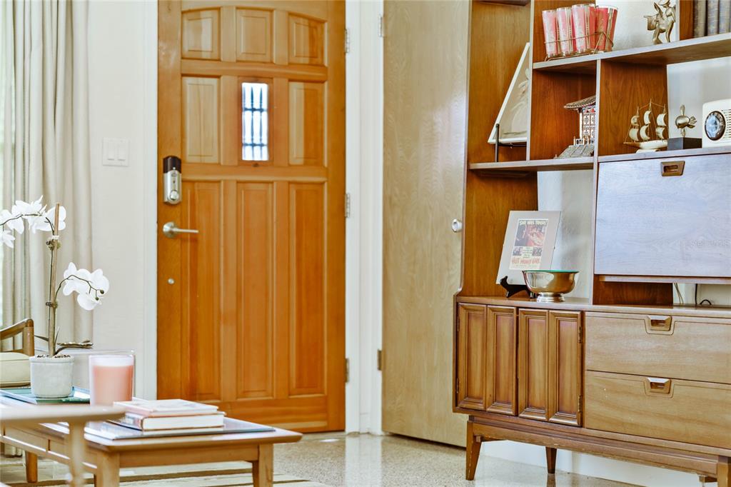 A wooden front door stands next to a mid-century modern shelving unit in a room — 809 E 15TH AVENUE, NEW SMYRNA BEACH, FL