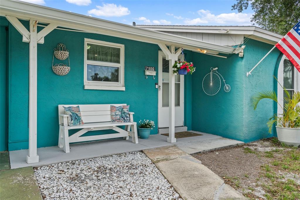A teal house exterior features a white bench, a front door, and a decorative bicycle — 7906 WOODVINE CIRCLE, TAMPA, FL