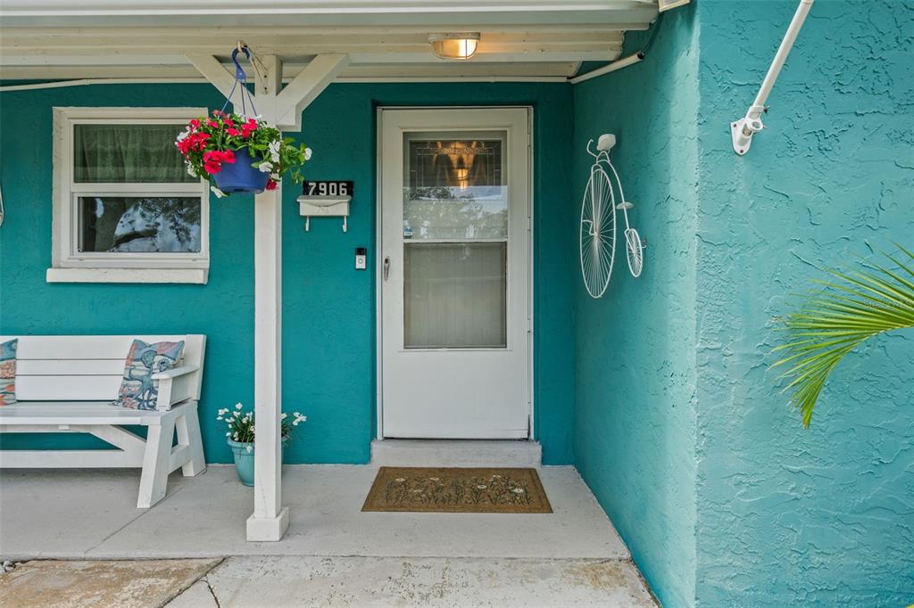A turquoise exterior wall features a white front door, a bench, and a hanging planter — 7906 WOODVINE CIRCLE, TAMPA, FL