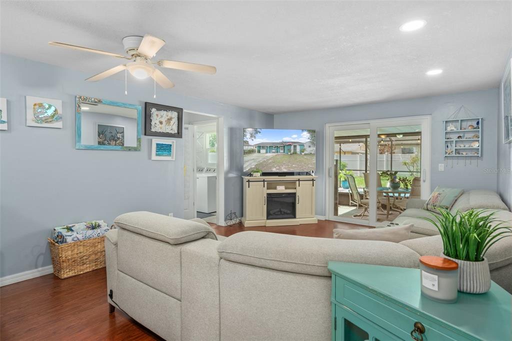 A living room with light blue walls, wood flooring, a sectional sofa, and sliding glass doors — 7906 WOODVINE CIRCLE, TAMPA, FL