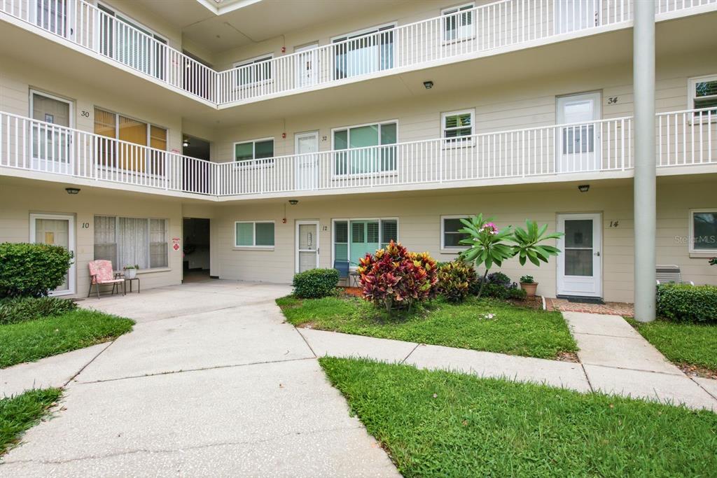 A multi-story apartment building exterior features white railings, numbered doors, and a landscaped courtyard — 2440 WORLD PARKWAY BOULEVARD UNIT 34, CLEARWATER, FL