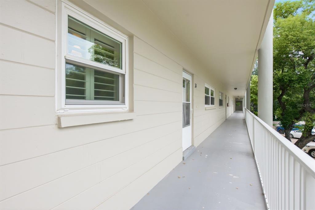 A long, covered outdoor walkway runs along the side of a beige apartment building — 2440 WORLD PARKWAY BOULEVARD UNIT 34, CLEARWATER, FL