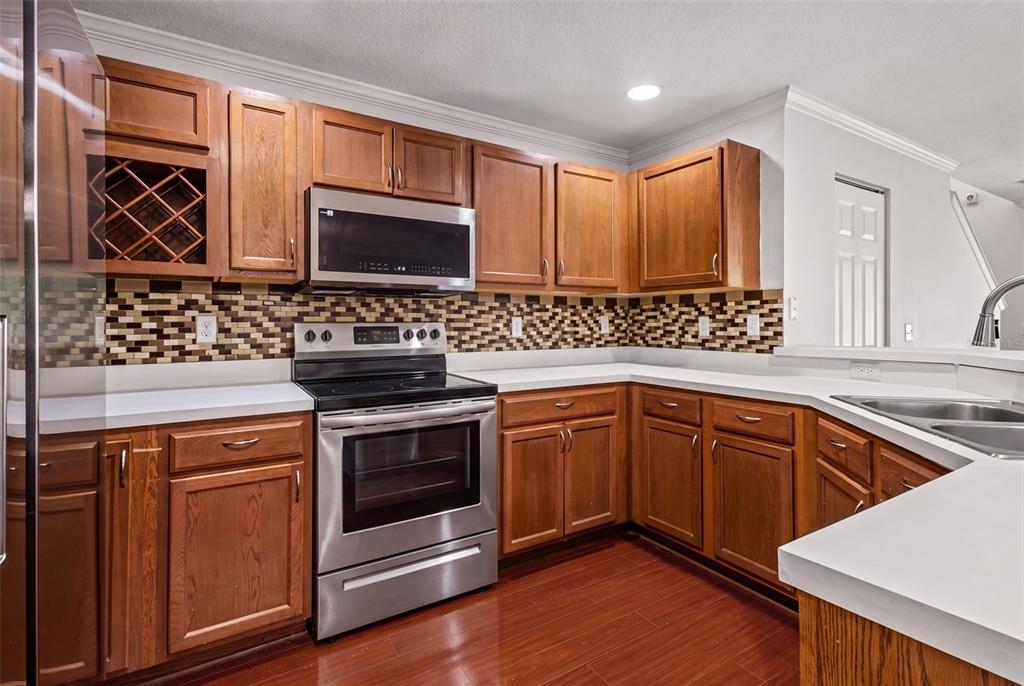 A kitchen features wood cabinets, stainless steel appliances, a mosaic tile backsplash, and white countertops — 2972 ROYAL TUSCAN LANE, VALRICO, FL