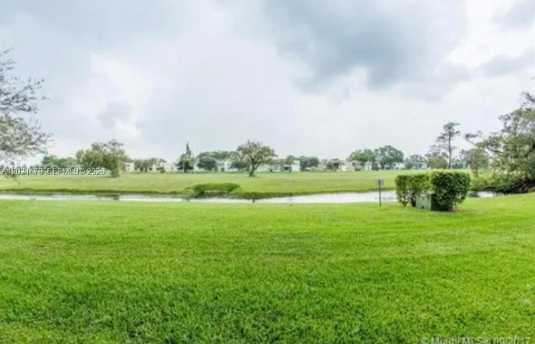 A grassy lawn overlooks a small pond with trees and buildings in the distance — 7396 NW 18th St # 104, Margate FL 33063, MARGATE, FL