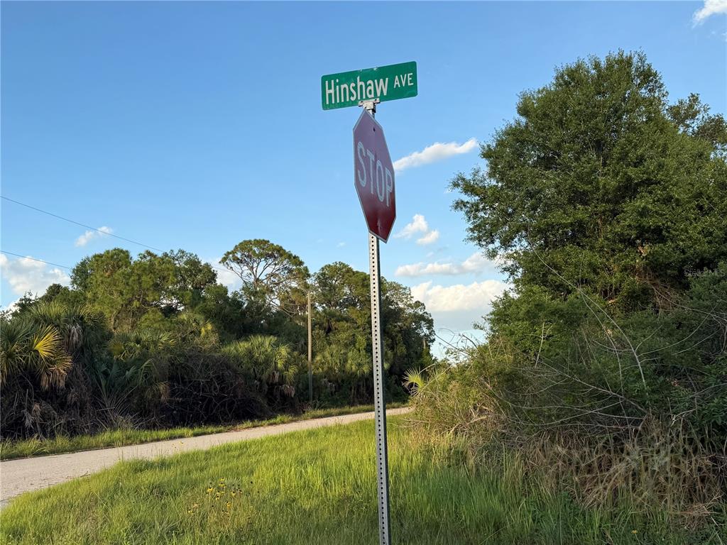 A stop sign and a street sign labeled Hinshaw Ave stand beside a dirt road — Lot 24 HINSHAW AVENUE, NORTH PORT, FL