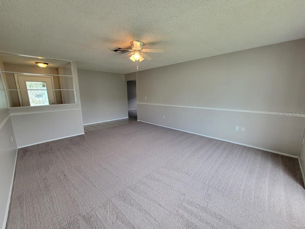 A carpeted living room features a ceiling fan, chair rail molding, and a built-in shelf — 12639 SKIPPER LANE, HUDSON, FL