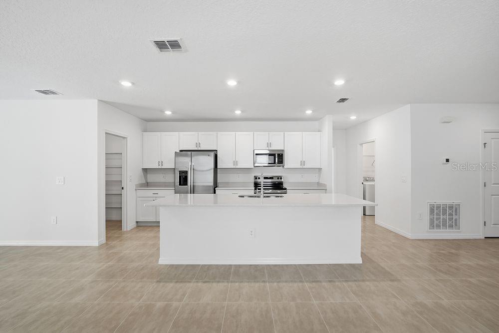 A modern kitchen features white cabinetry, a large central island, and light-colored tile flooring — 13520 TROPICAL BREEZE WAY, HUDSON, FL