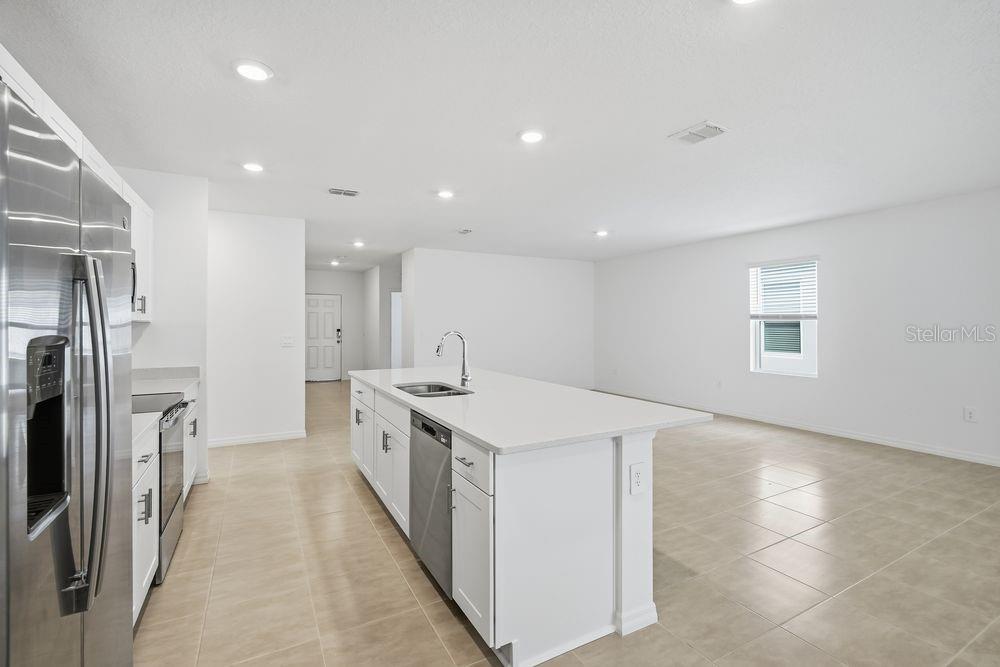 A modern kitchen features a white island, stainless steel appliances, and light tile flooring — 13520 TROPICAL BREEZE WAY, HUDSON, FL