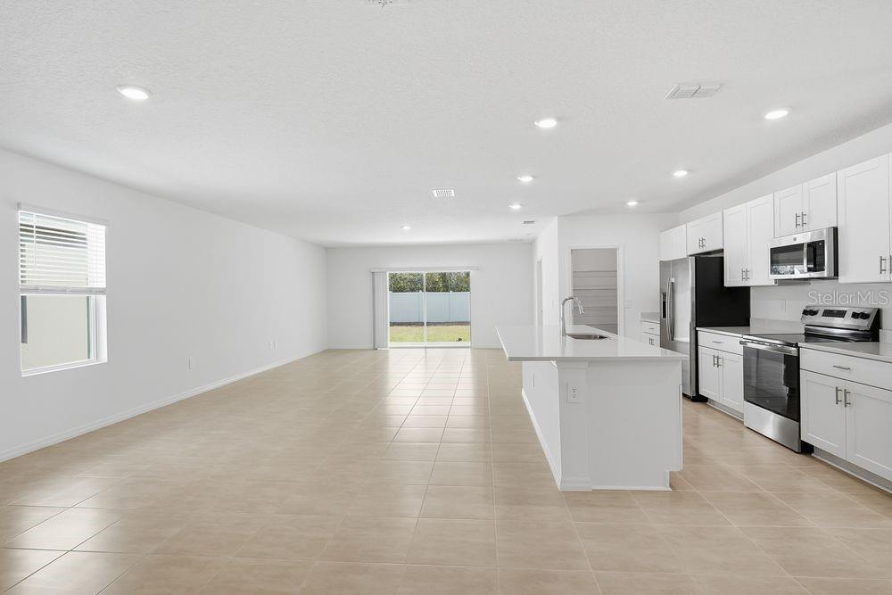 A bright, open-concept kitchen and living area with white cabinets, stainless appliances, and tile flooring — 13520 TROPICAL BREEZE WAY, HUDSON, FL