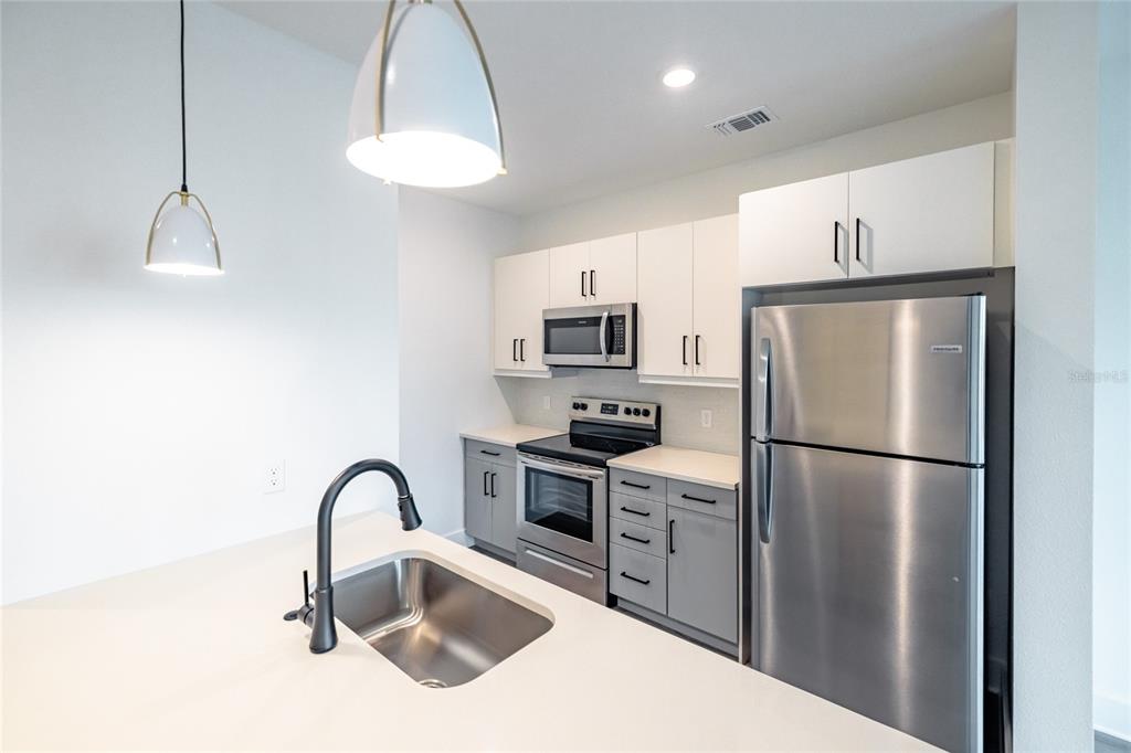 A kitchen features white upper cabinets, grey lower cabinets, stainless steel appliances, and a sink island — 1420 LAKEFRONT DRIVE UNIT ST-3303, SARASOTA, FL