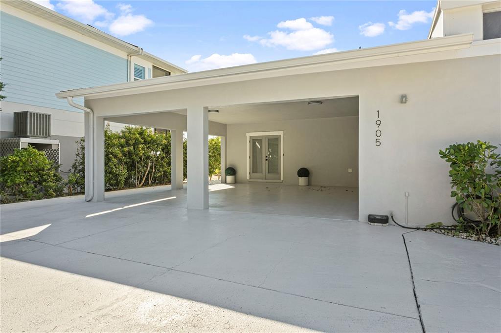 A covered carport with a concrete floor leads to a set of double glass doors — 1905 4TH STREET W, PALMETTO, FL