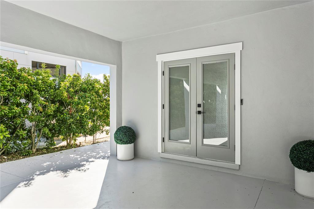 A gray patio features double glass doors, white trim, and two potted topiary plants — 1905 4TH STREET W, PALMETTO, FL