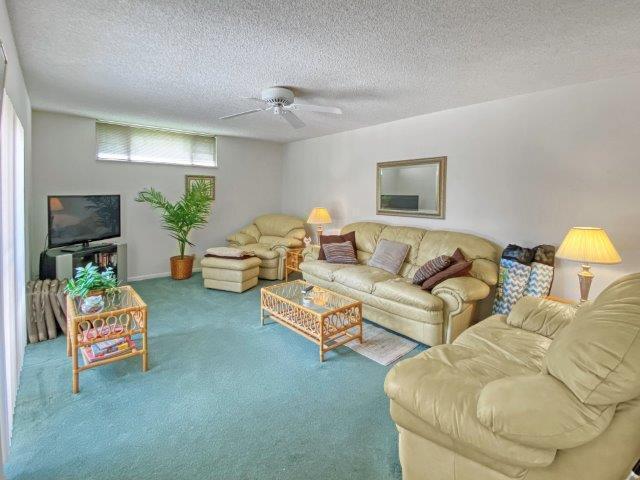 A living room features a beige sofa, matching armchair, teal carpeting, and a ceiling fan — 62 Springdale Circle, Palm Springs FL 33461, PALM SPRINGS, FL