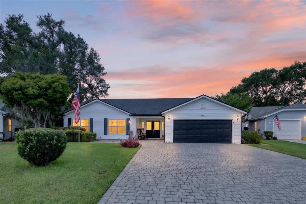 A single-story house with a paved driveway, dark garage door, and a sunset sky background — 25102 MERIWEATHER ROAD, LEESBURG, FL