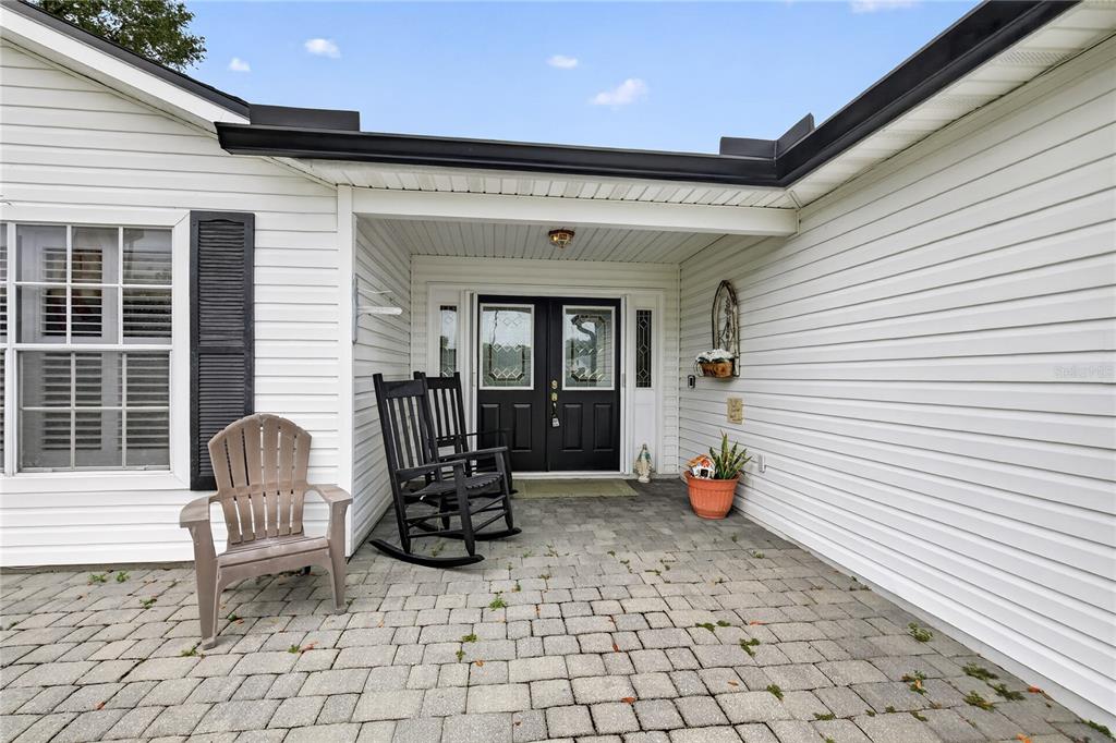 A paved front porch features two rocking chairs, a plastic chair, and black double doors — 25102 MERIWEATHER ROAD, LEESBURG, FL