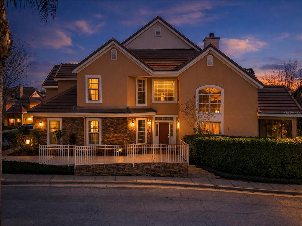 A two-story house with a stone facade, white fence, and tiled roof at dusk — 7000 STONEHEDGE DRIVE UNIT 156, ORLANDO, FL