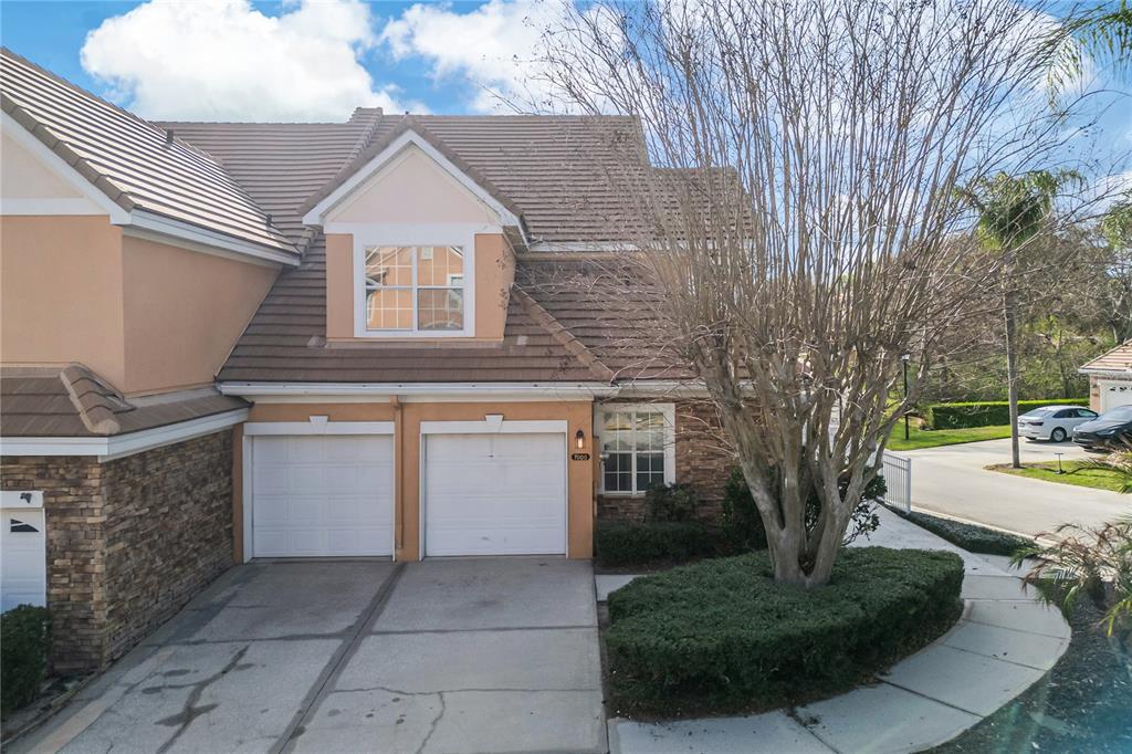 A two-story townhouse features a two-car garage, stone veneer accents, and a large bare tree — 7000 STONEHEDGE DRIVE UNIT 156, ORLANDO, FL