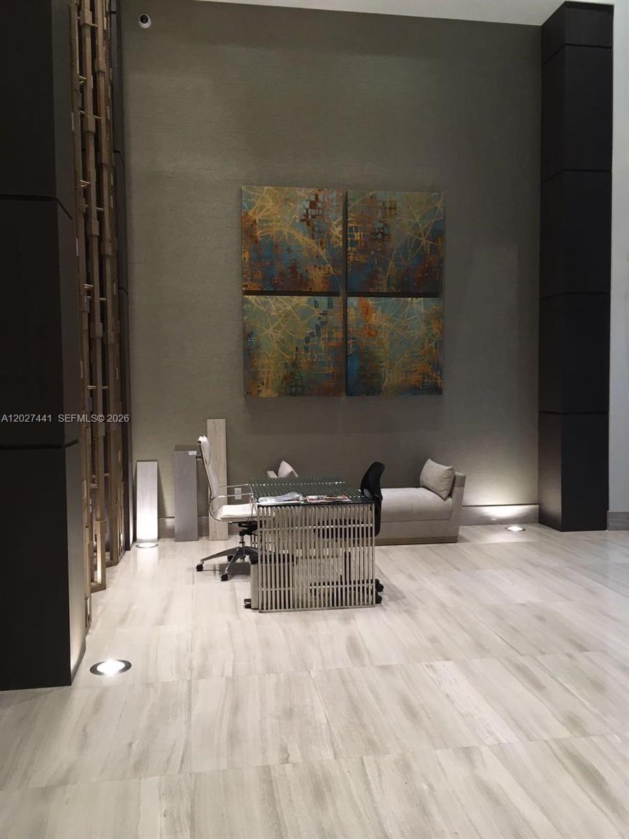 A modern office space features a glass desk, a small sofa, and abstract wall art — MIAMI, FL