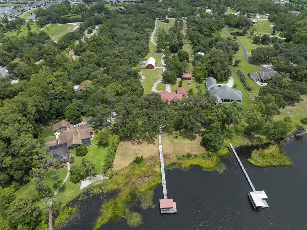 An aerial view shows two waterfront houses with private docks, a barn, and wooded grounds — 2700 ZUNI ROAD, ST CLOUD, FL