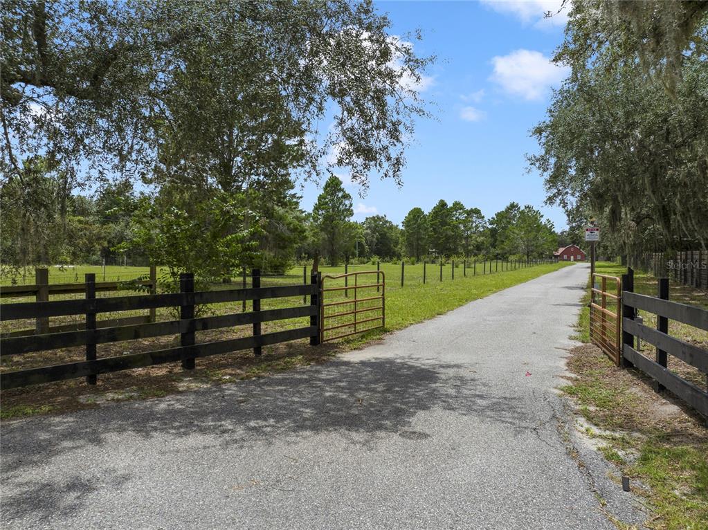 A paved driveway leads through an open metal gate toward a red barn in the distance — 2700 ZUNI ROAD, ST CLOUD, FL