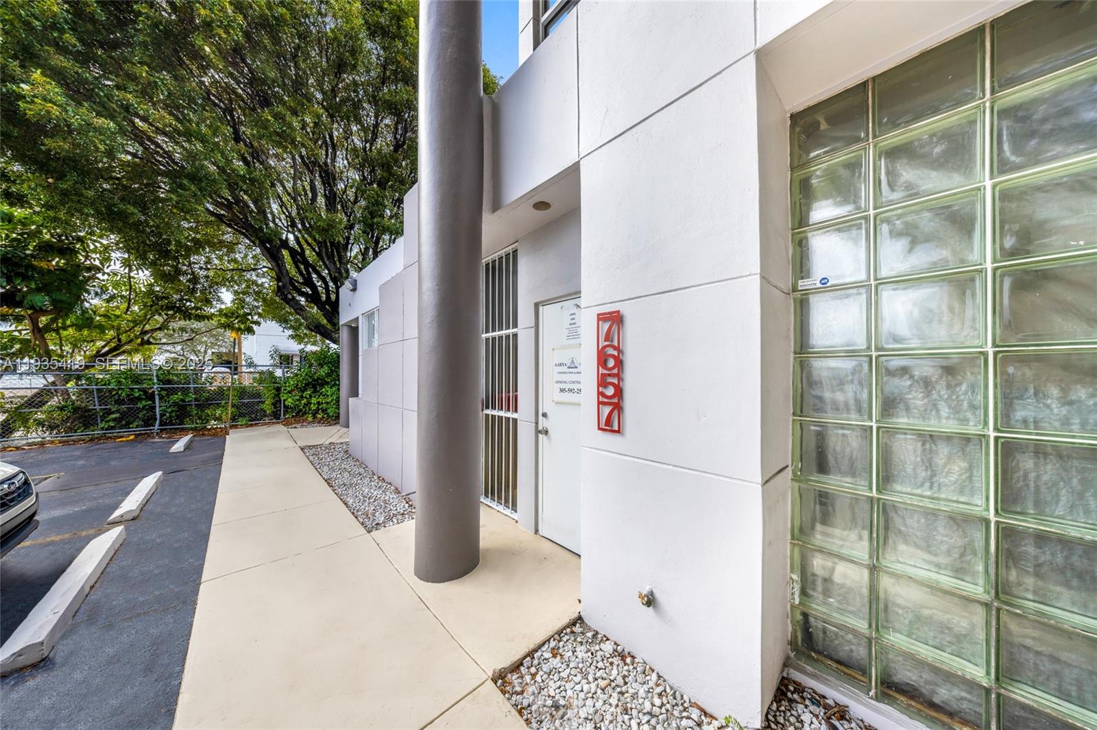The exterior of a building features a white wall, glass block windows, and a numbered sign — 7657 NW 50th St, Miami FL 33166, MIAMI, FL
