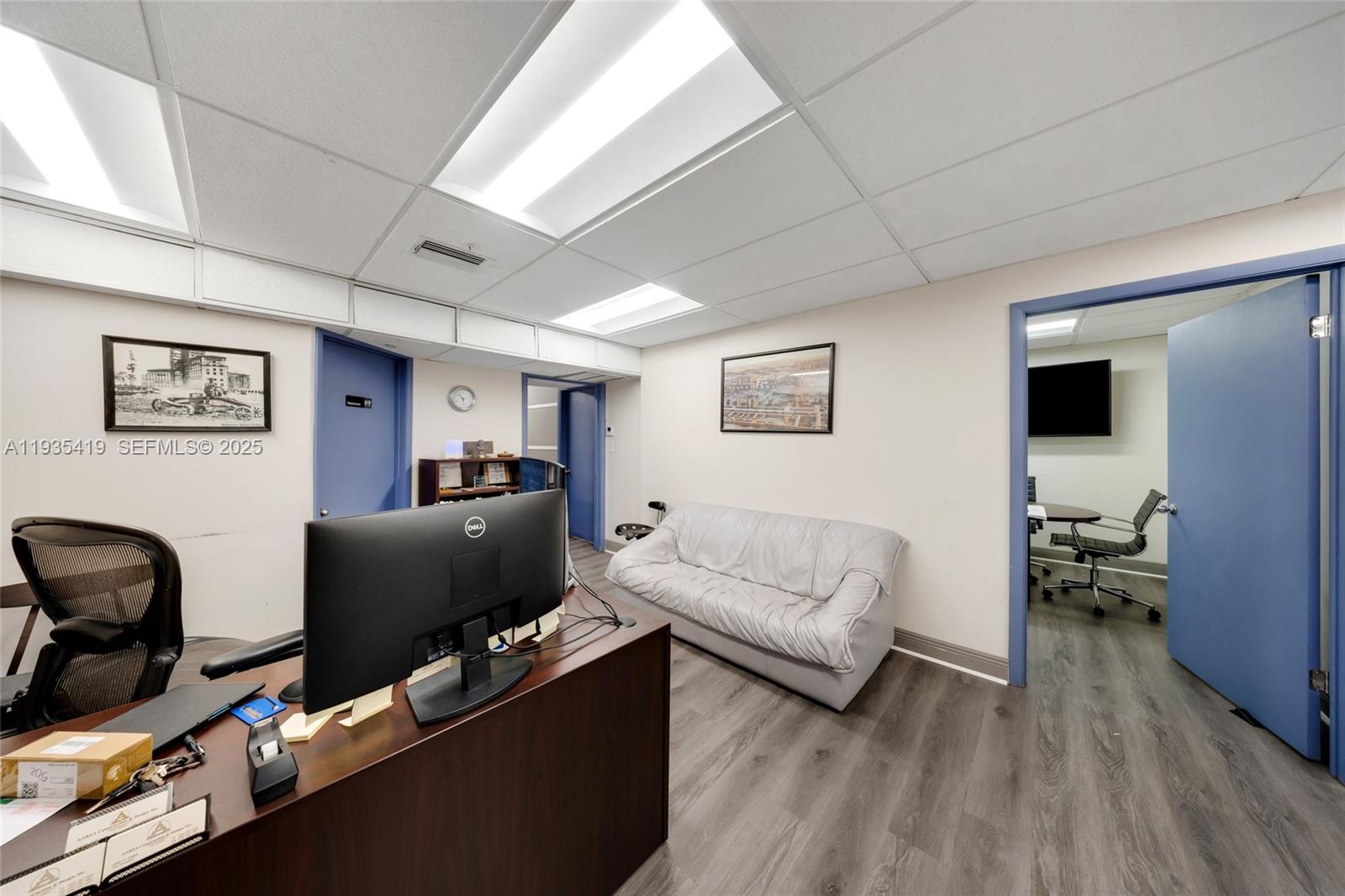 An office space features a desk with a computer, a sofa, and blue doors — 7657 NW 50th St, Miami FL 33166, MIAMI, FL