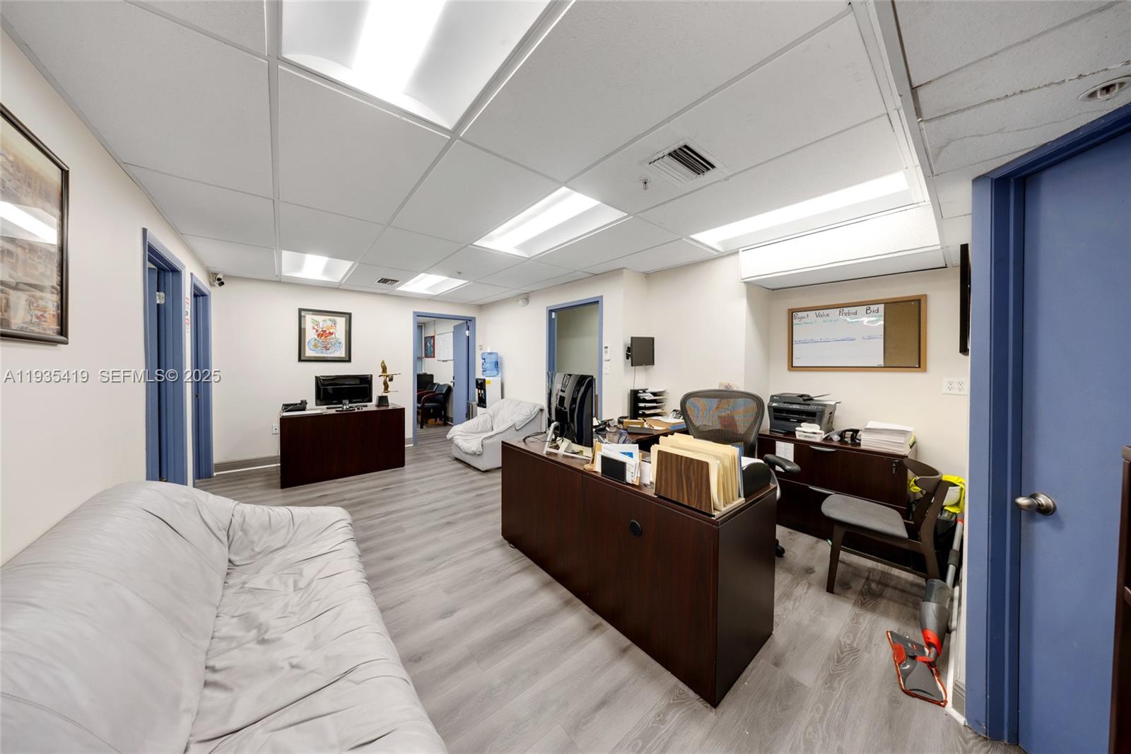 An office space features a desk, a sofa, wood-look flooring, and a drop ceiling — 7657 NW 50th St, Miami FL 33166, MIAMI, FL