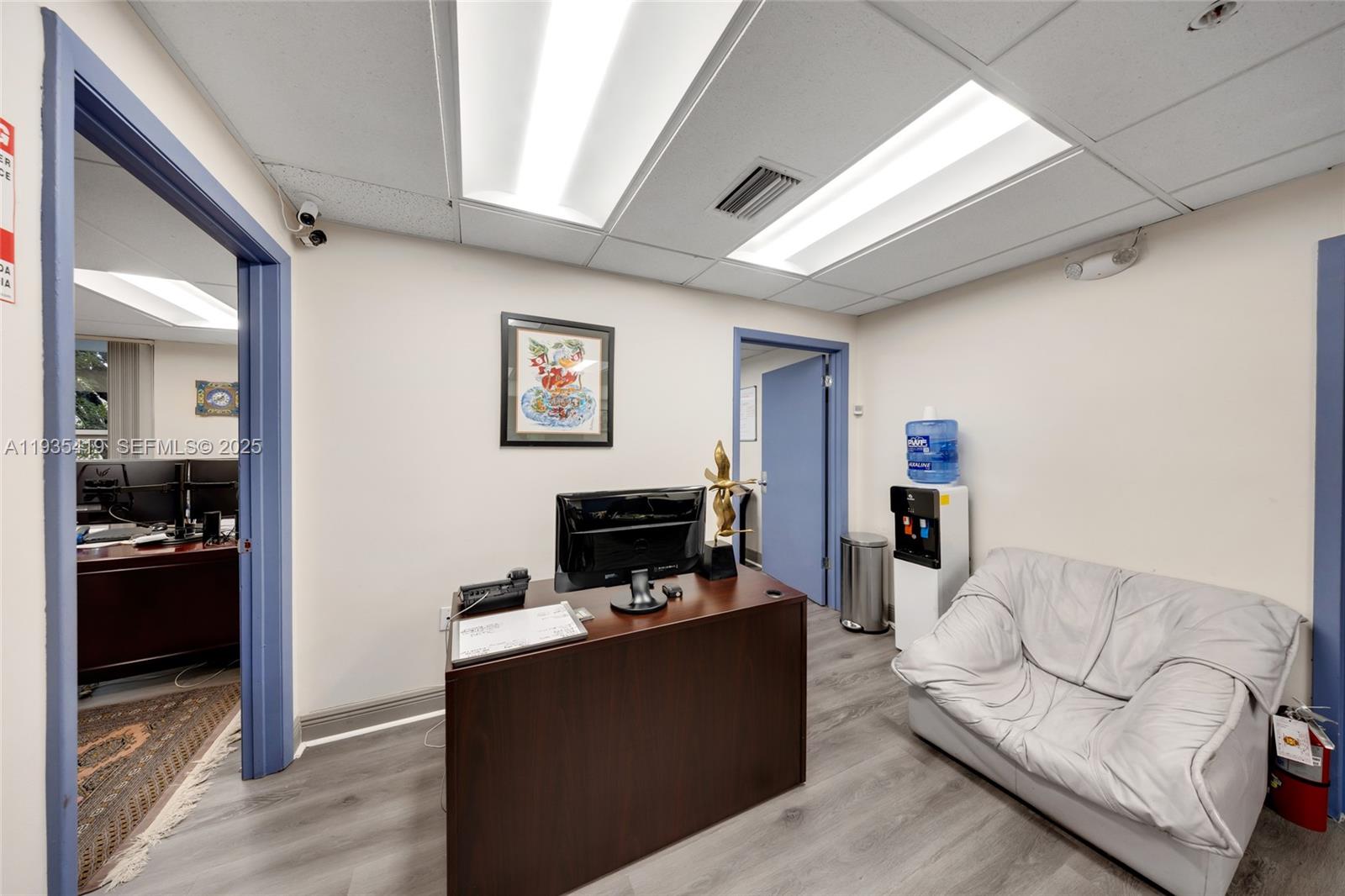 An office space features a dark wood desk, a white sofa, and a water cooler — 7657 NW 50th St, Miami FL 33166, MIAMI, FL