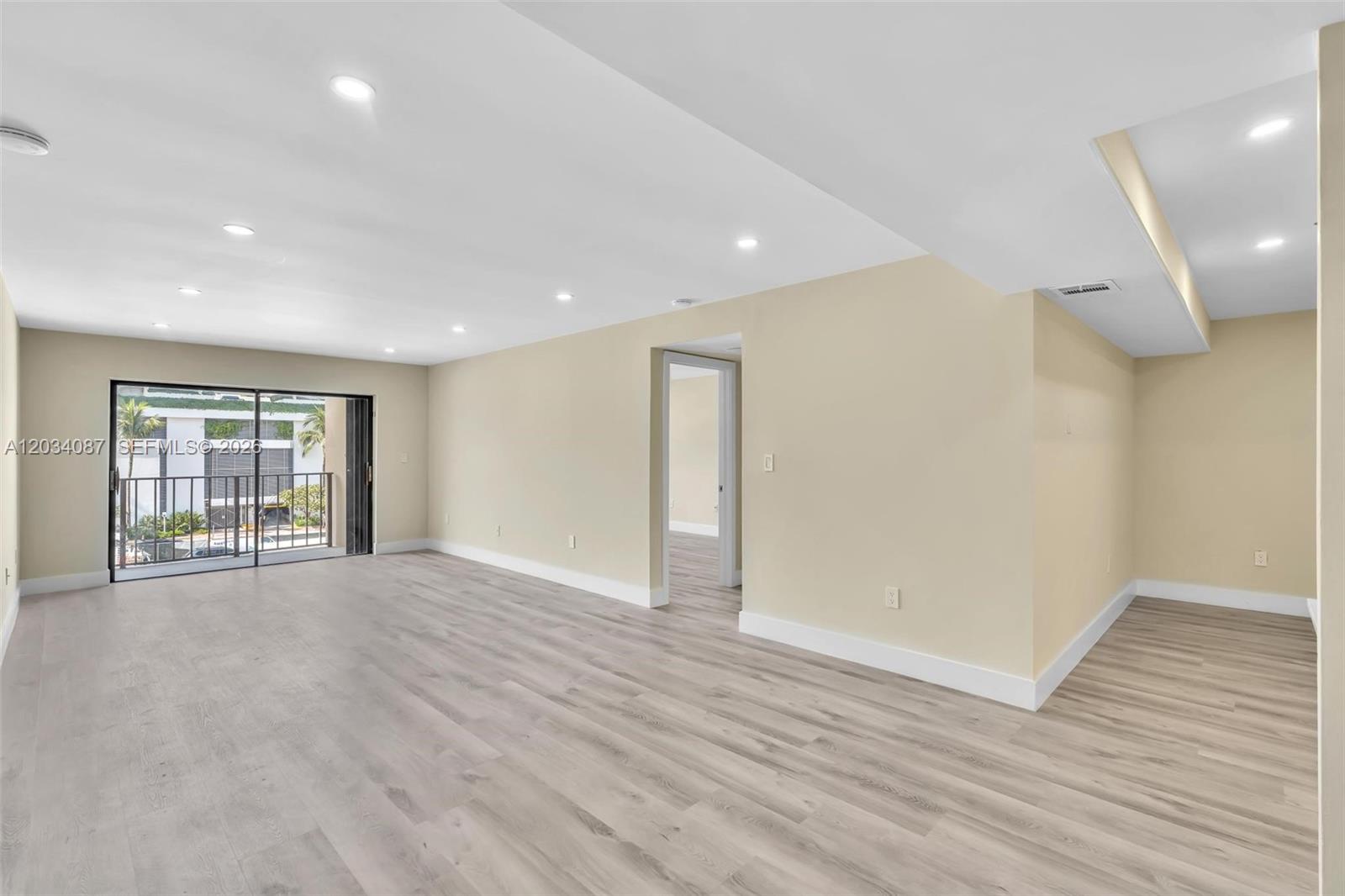 An empty living room features light wood-look flooring, beige walls, recessed lighting, and a balcony — 9124 Collins Ave # 304, Surfside FL 33154, SURFSIDE, FL