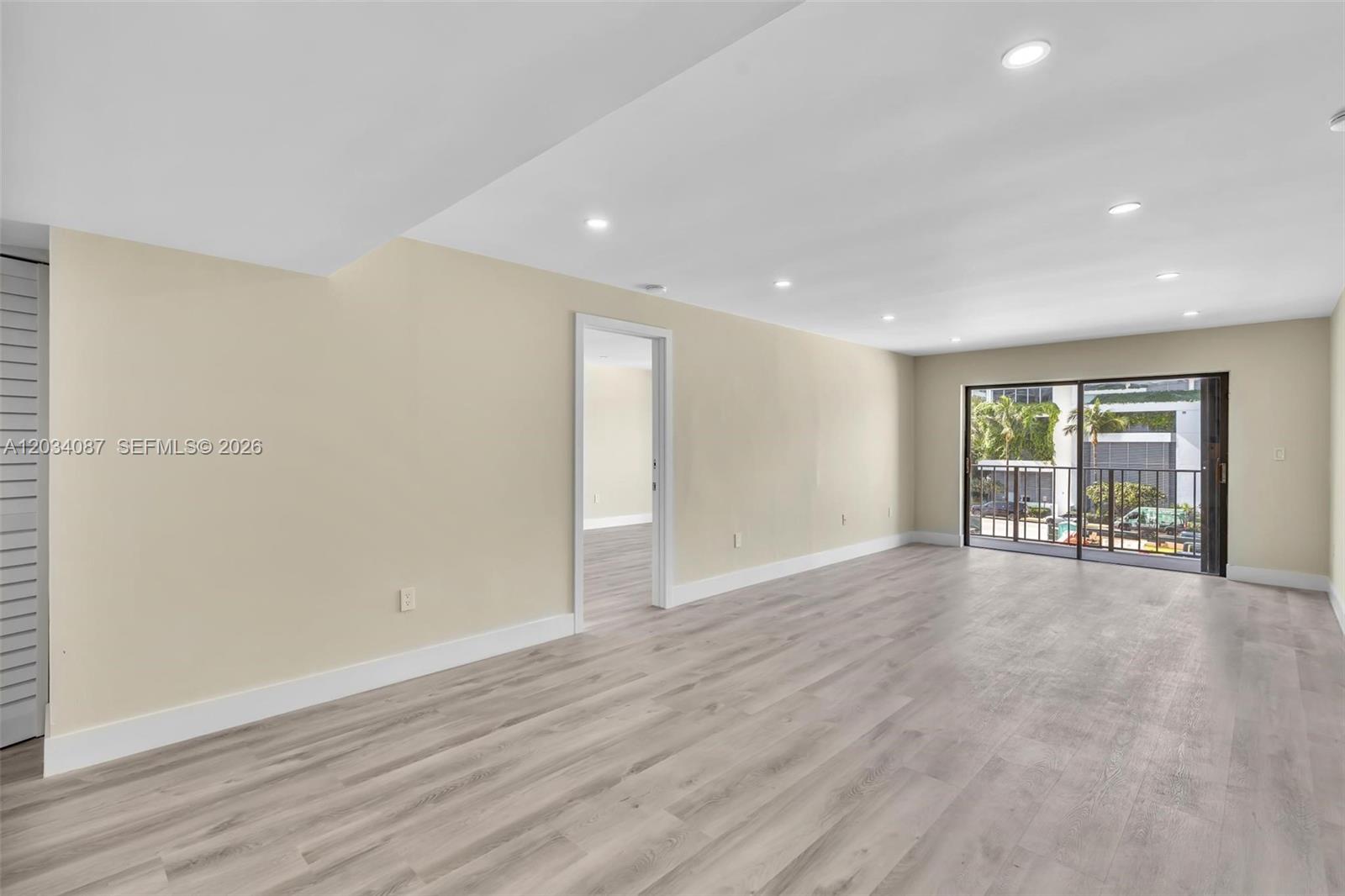 An empty room features light wood-look flooring, recessed lighting, and a sliding glass door balcony — 9124 Collins Ave # 304, Surfside FL 33154, SURFSIDE, FL