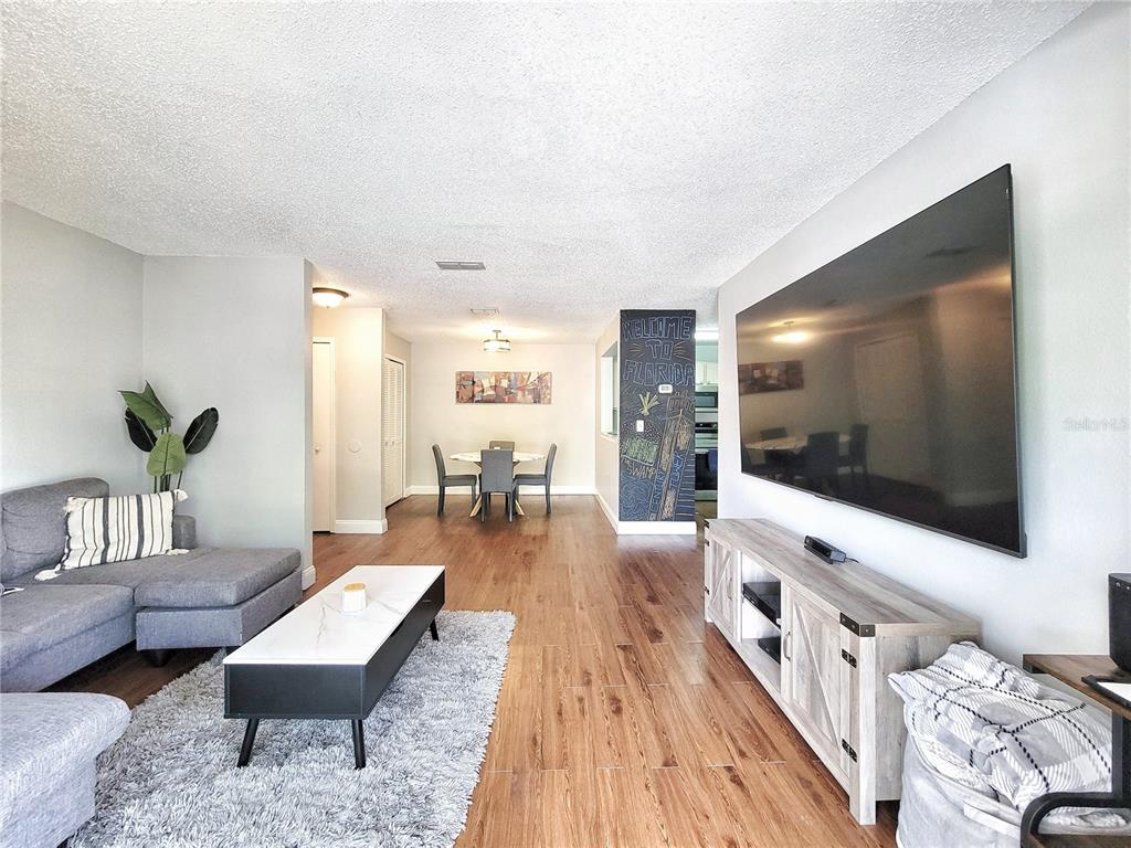 A living room with wood-look flooring, a grey sectional, and a large wall-mounted television — 3705 SW 27TH STREET UNIT 527, GAINESVILLE, FL