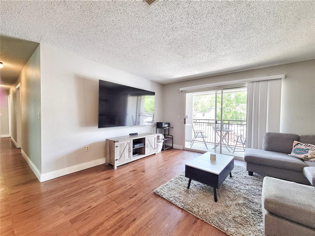 A living room with wood-look flooring, a wall-mounted television, and a sliding glass balcony door — 3705 SW 27TH STREET UNIT 527, GAINESVILLE, FL