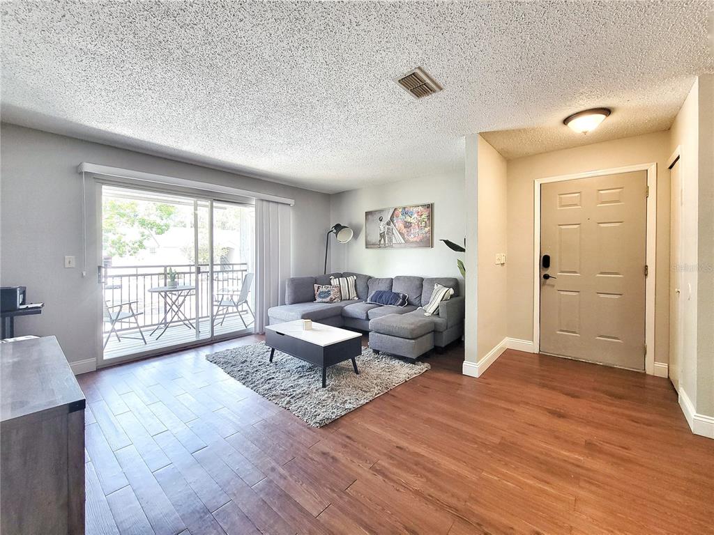 A living room features wood-look flooring, a gray sectional sofa, and a sliding glass door — 3705 SW 27TH STREET UNIT 527, GAINESVILLE, FL