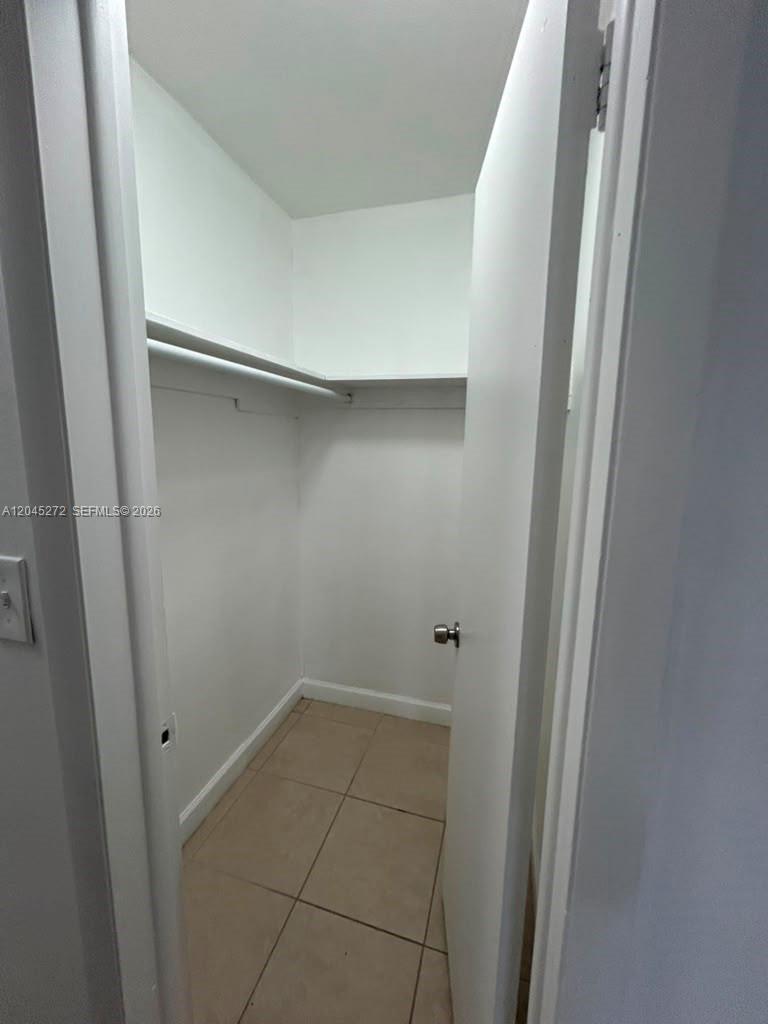 A small walk-in closet features white walls, a single shelf, and light-colored tile flooring — 2435 Van Buren St APT 1B, Hollywood FL 33020, HOLLYWOOD, FL