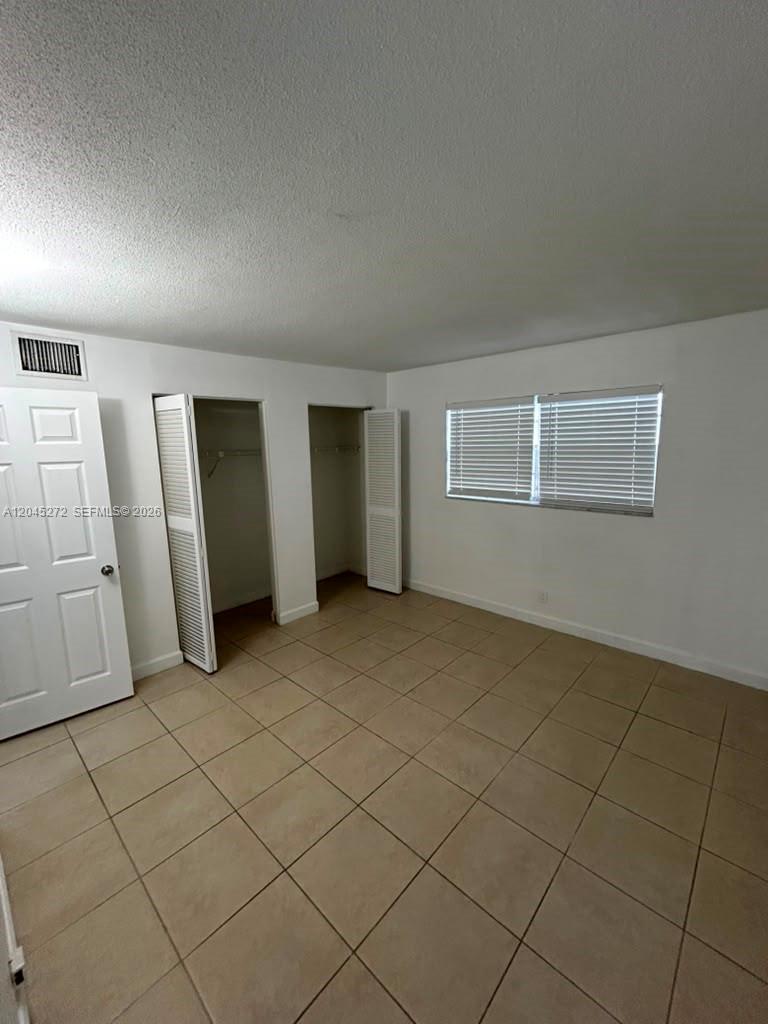 An empty bedroom features white walls, tile flooring, two open closets, and a window with blinds — 2435 Van Buren St APT 1B, Hollywood FL 33020, HOLLYWOOD, FL