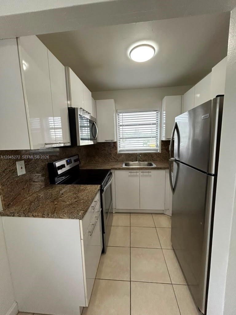 A galley kitchen features white cabinets, granite countertops, stainless steel appliances, and tile flooring — 2435 Van Buren St APT 1B, Hollywood FL 33020, HOLLYWOOD, FL