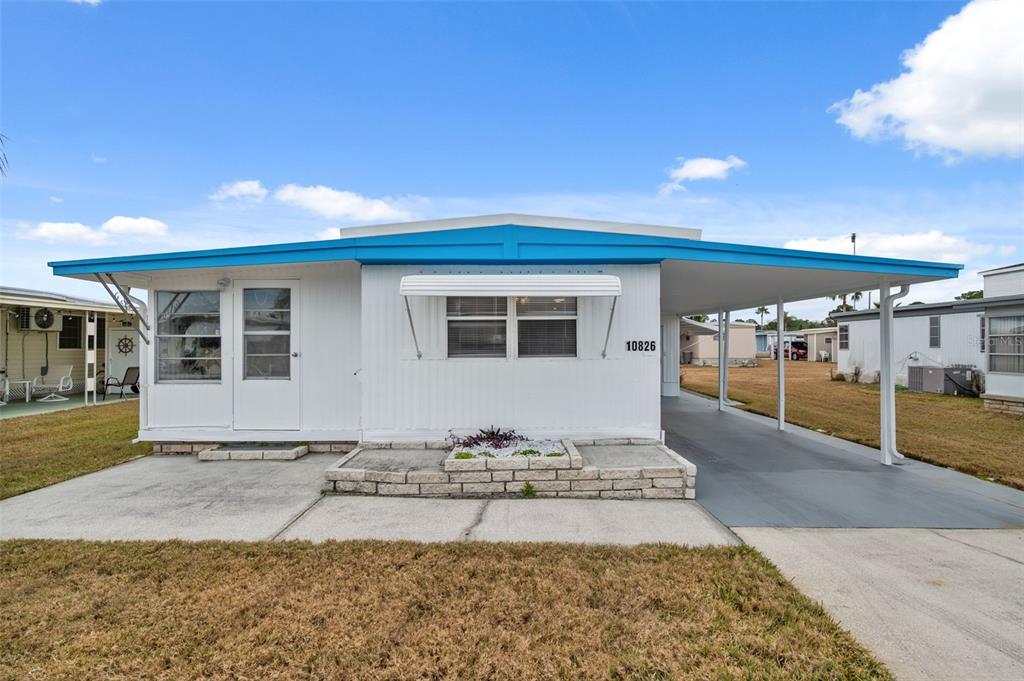 A white mobile home with a blue roof and an attached carport sits on a lot — 10826 TIOGA DRIVE, PORT RICHEY, FL