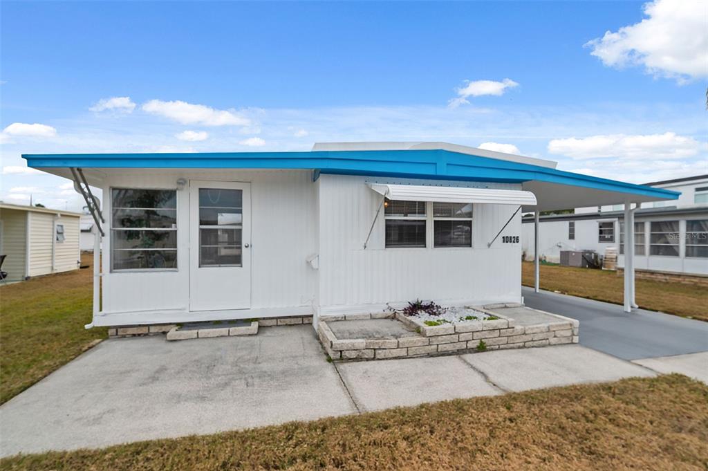 A white mobile home features a blue roof trim, a concrete driveway, and a small planter — 10826 TIOGA DRIVE, PORT RICHEY, FL