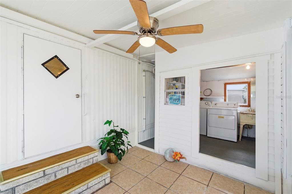 A tiled porch features a ceiling fan, a potted plant, and a view into a laundry room — 10826 TIOGA DRIVE, PORT RICHEY, FL