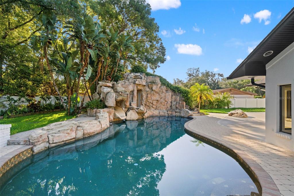 A backyard swimming pool features a large rock waterfall and a stone paver patio — 2521 LAKE ELLEN DRIVE, TAMPA, FL
