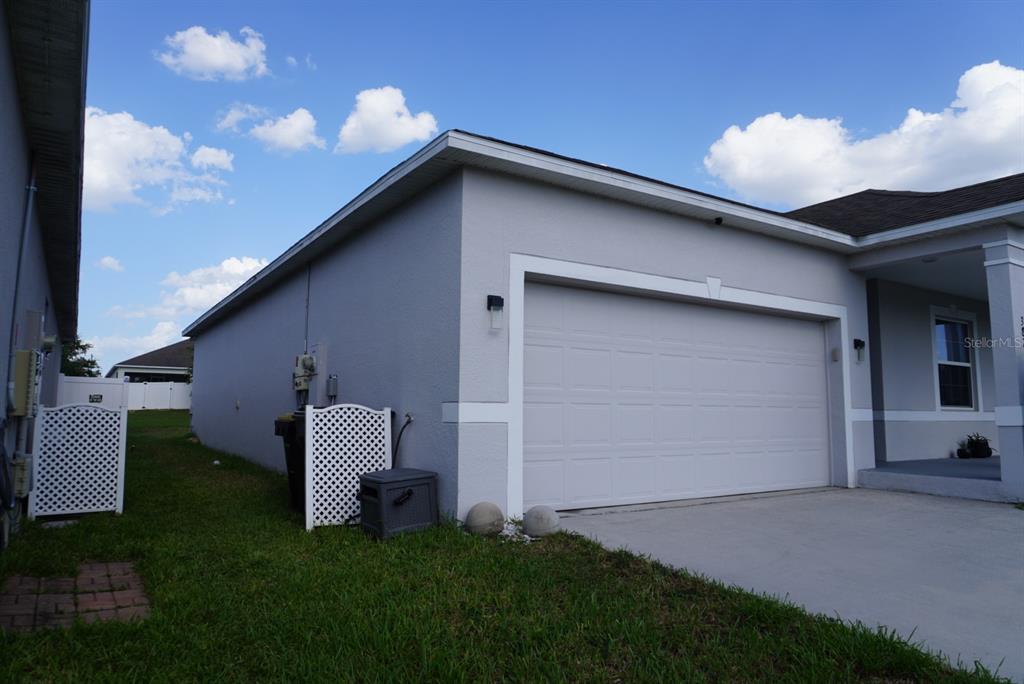 The exterior of a house features a two-car garage, a white lattice gate, and lawn — 387 PINECREST LOOP, DAVENPORT, FL