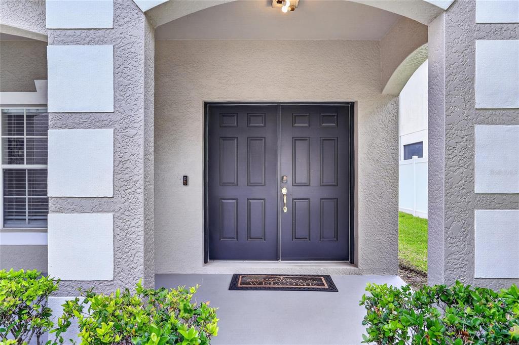 A covered entryway features a dark double front door with a welcome mat — 8821 N RIVER ROAD, TAMPA, FL