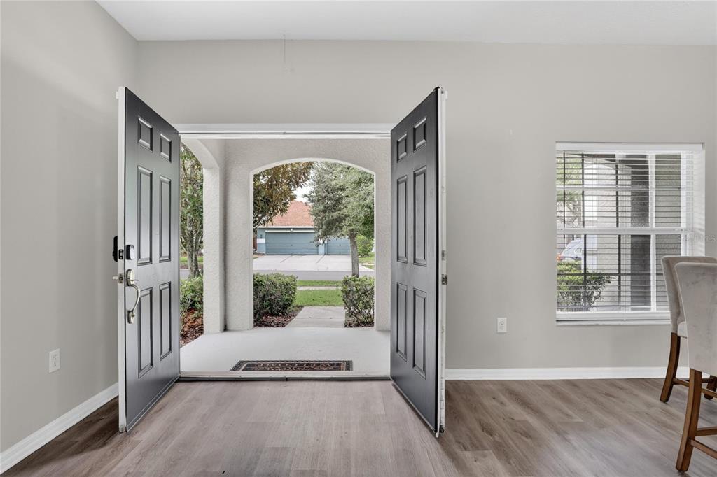 An open double front door reveals a covered entryway and a view of a suburban street — 8821 N RIVER ROAD, TAMPA, FL