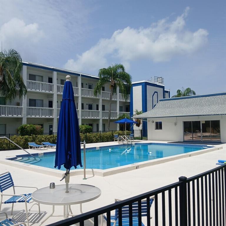 A rectangular swimming pool sits in front of a multi-story apartment building with balconies — 350 79TH AVENUE N UNIT 134, ST PETERSBURG, FL