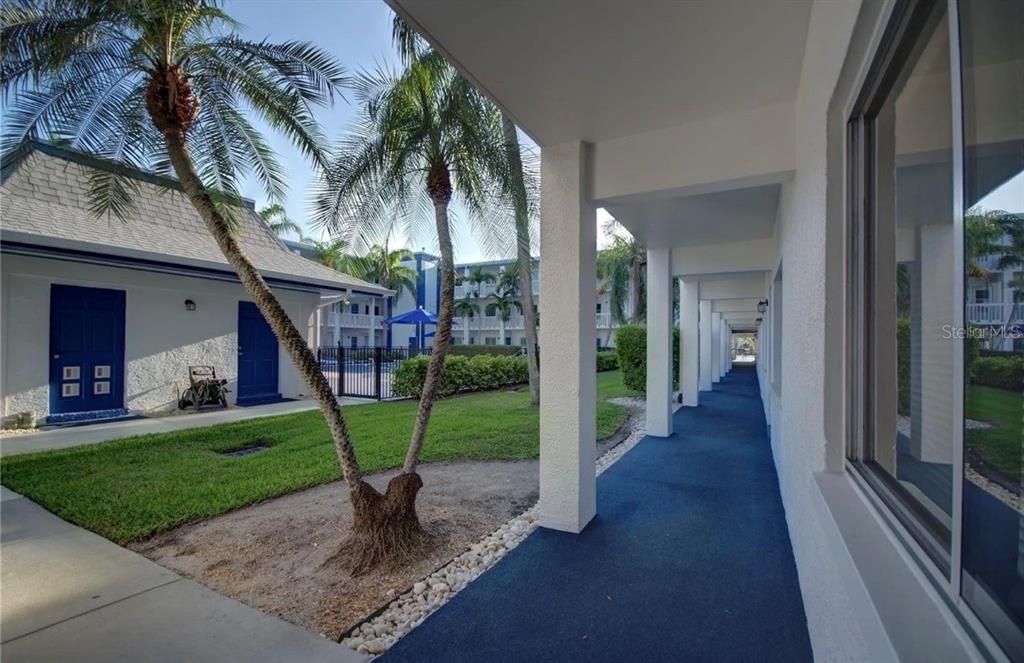 A covered outdoor walkway with blue flooring runs alongside a building with palm trees — 350 79TH AVENUE N UNIT 134, ST PETERSBURG, FL