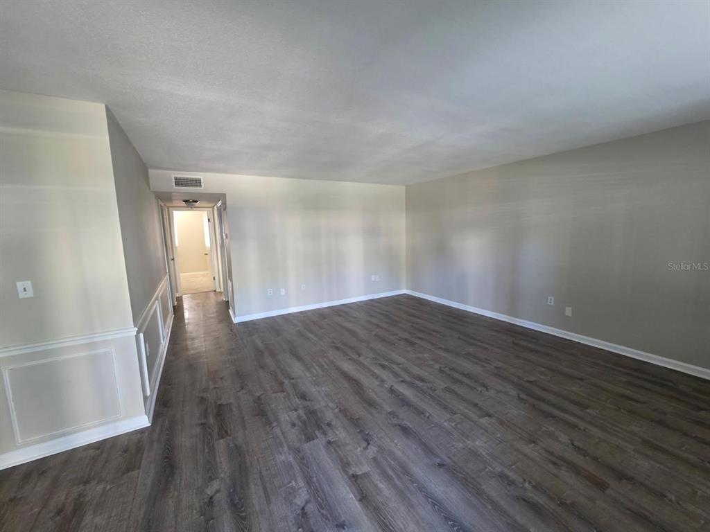 An empty room features wood-look flooring, light gray walls, and a hallway leading elsewhere — 350 79TH AVENUE N UNIT 134, ST PETERSBURG, FL