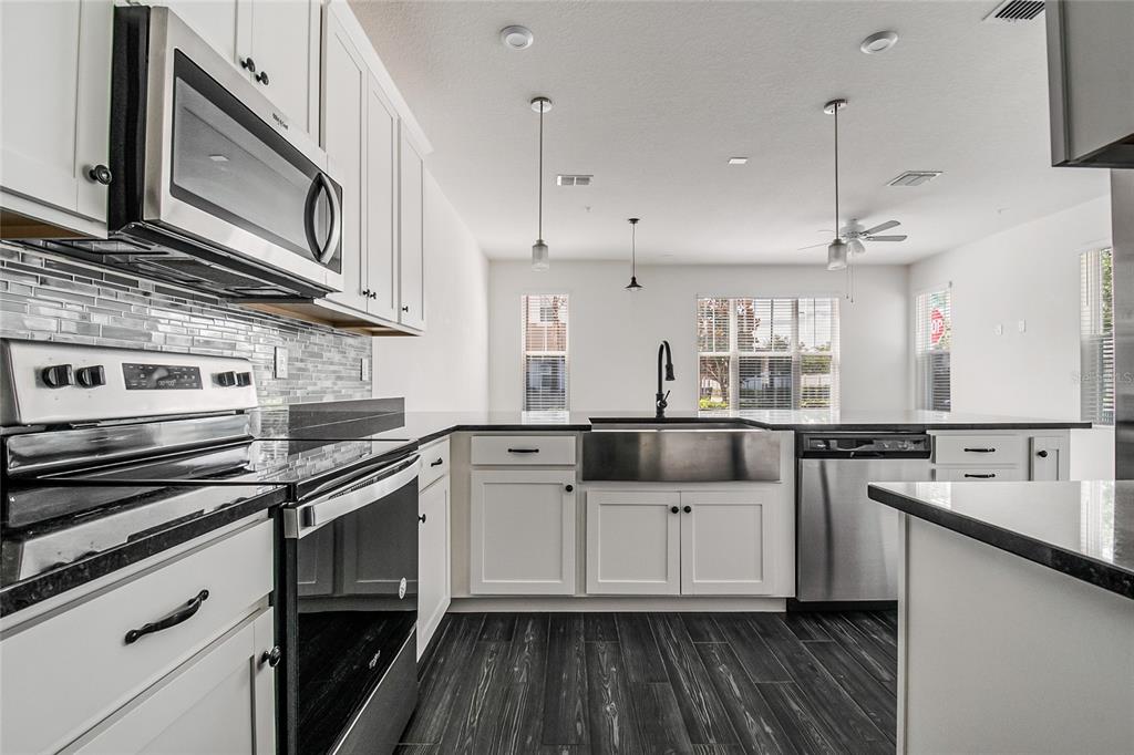 A modern kitchen features white cabinetry, stainless steel appliances, a farmhouse sink, and dark flooring — 9586 POPLAR RIDGE AVENUE, ORLANDO, FL