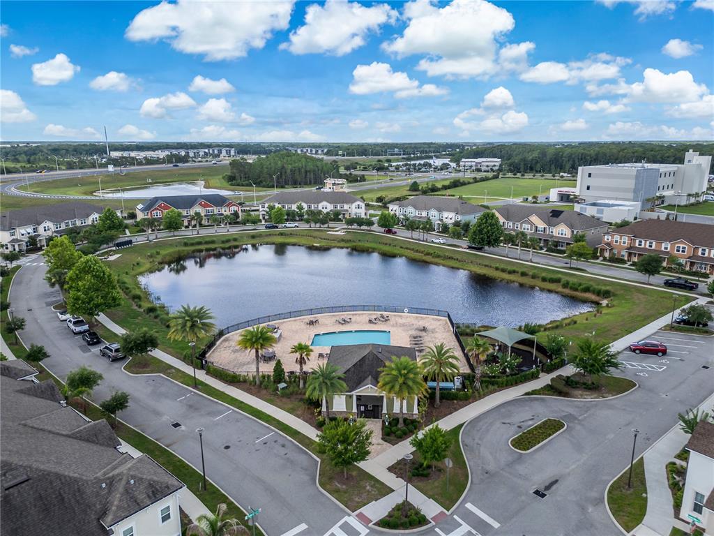 An aerial view shows a community swimming pool and clubhouse situated beside a large pond — 9586 POPLAR RIDGE AVENUE, ORLANDO, FL
