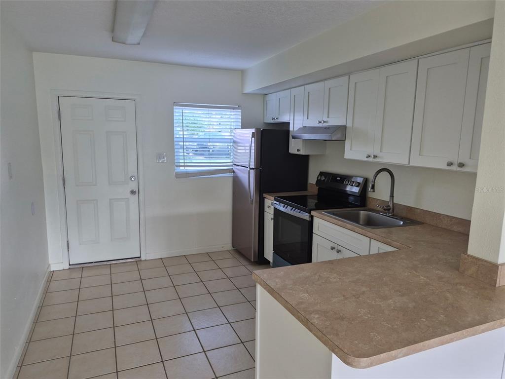 A kitchen features white cabinets, tan countertops, tile flooring, and stainless steel appliances — 13934 SOMMERS AVENUE, HUDSON, FL